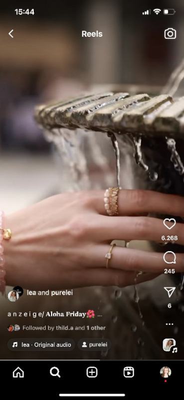 Screenshot eines Instagram Reels: Eine weibliche Hand mit Ringen und Armband vor einem Brunnen.