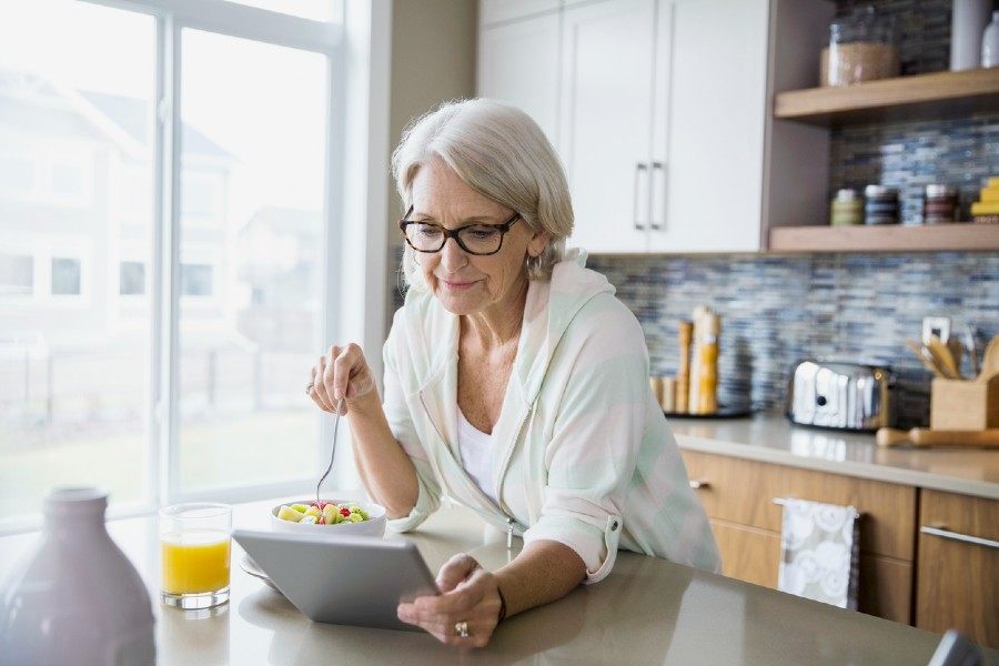 Eine ältere Frau schaut beim Frühstück auf ein Tablet.