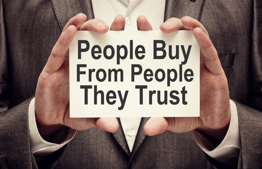 Ein Mann im Anzug hält einen Zettel mit der Aufschrift "People buy from People they Trust"