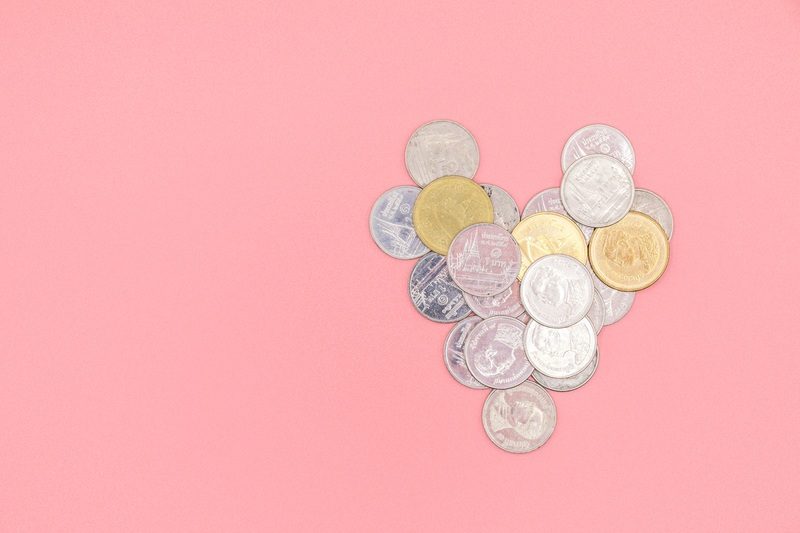 Münzen bilden Herzform auf pinken Hintergrund